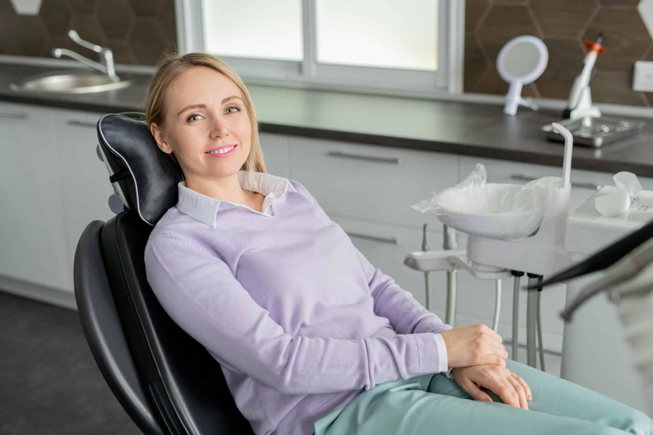 Pretty young smiling female patient of contemporary dentistry sitting in leather armchair and waiting for her doctor in clinics